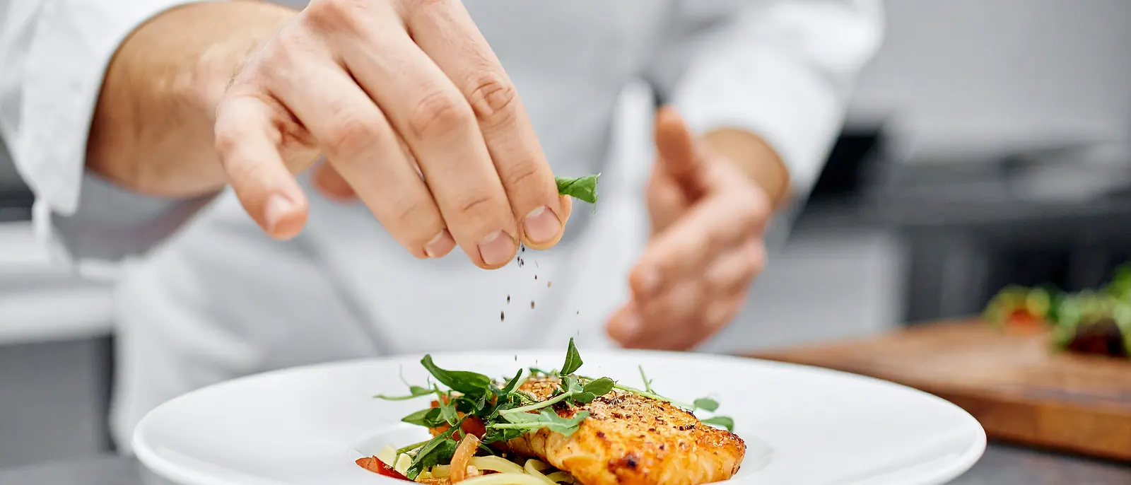 Manos de un cocinero emplatando un plato de salmón con hierbas frescas