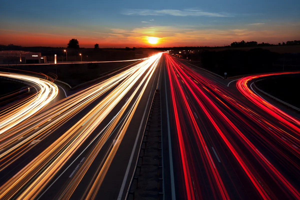 Estelas de luz de coches en una autopista al atardecer, fotografiadas con larga exposición