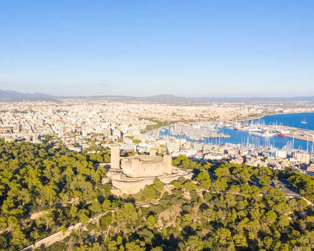 Castillo de Bellver entre pinares con la ciudad de Palma y su puerto al fondo